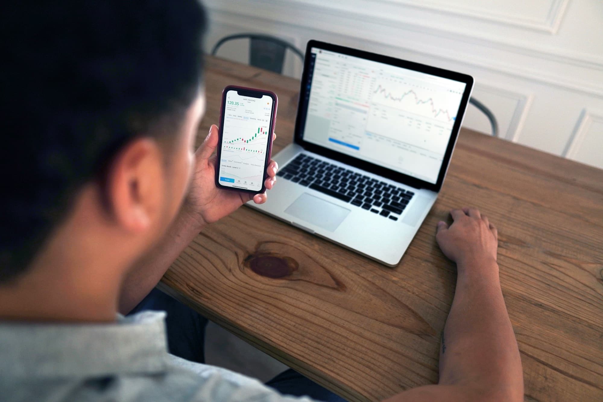 Investor reviewing markets on phone and laptop